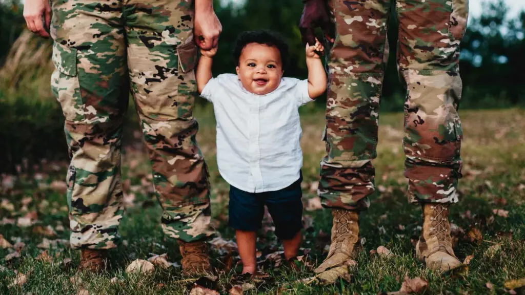 Two parents in uniform holding hands with a smiling baby