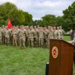 A speech being given at a podium in front of soldiers at attention.