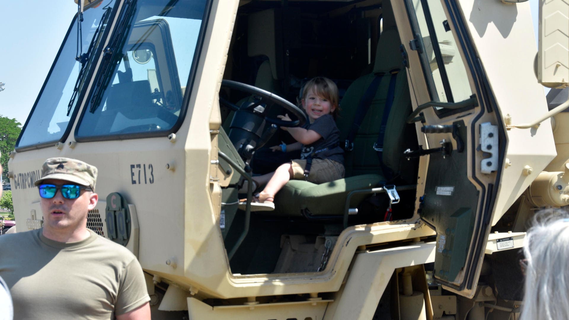 A smiling child in the drivers seat of a military vehicle
