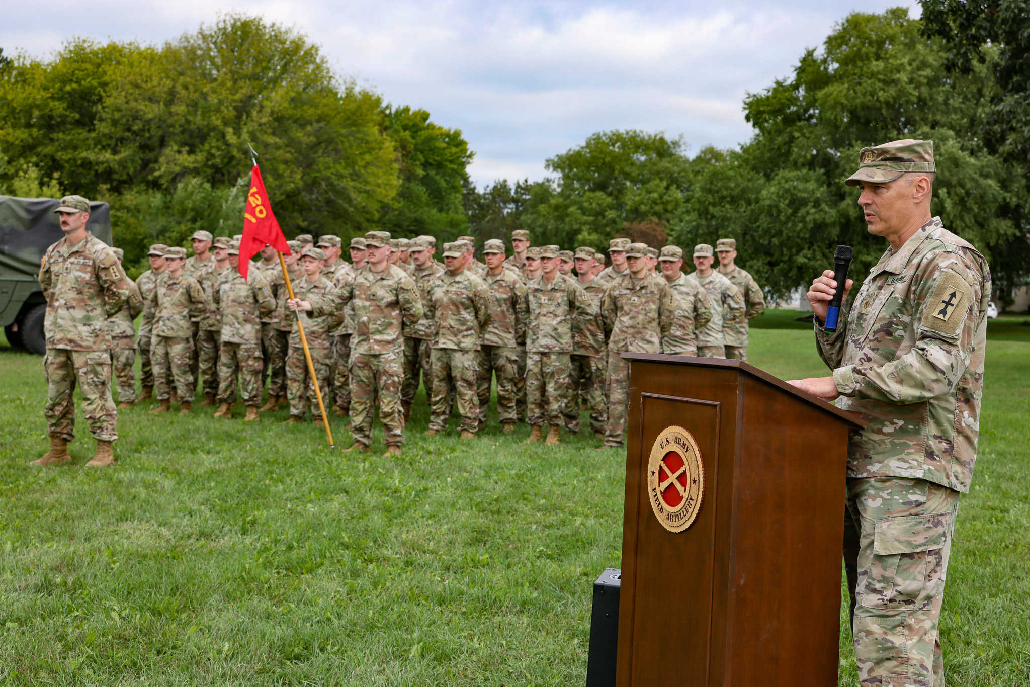 A speech being given at a podium in front of soldiers at attention.