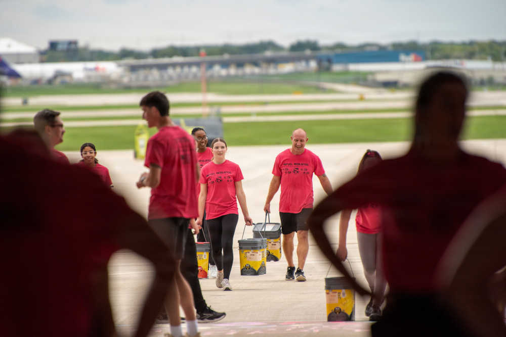 Service members carry containers filled with water as part of a group fitness exercise