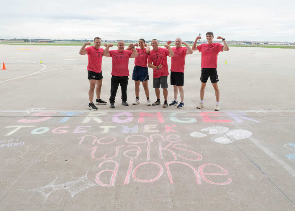 Service members pose in front of chalk artwork on the flight line