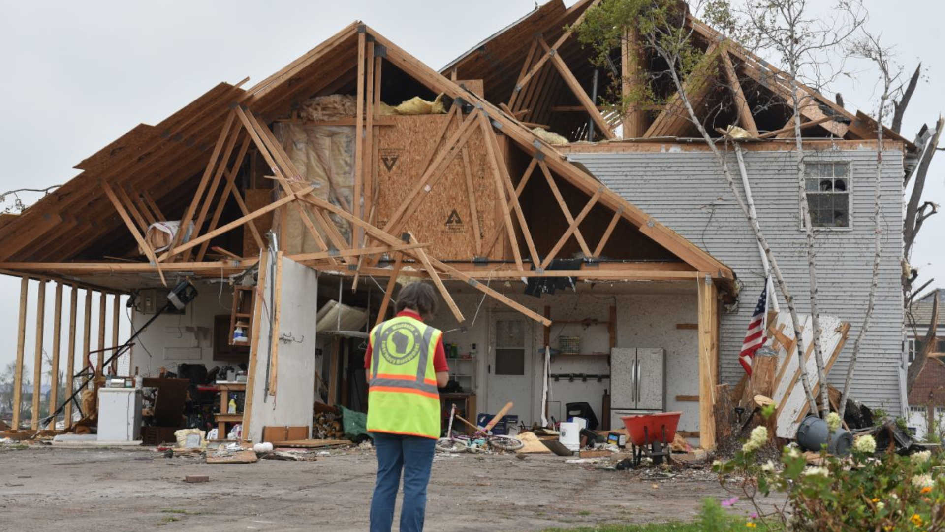 A woman standing in front of half a house with sever storm damage.