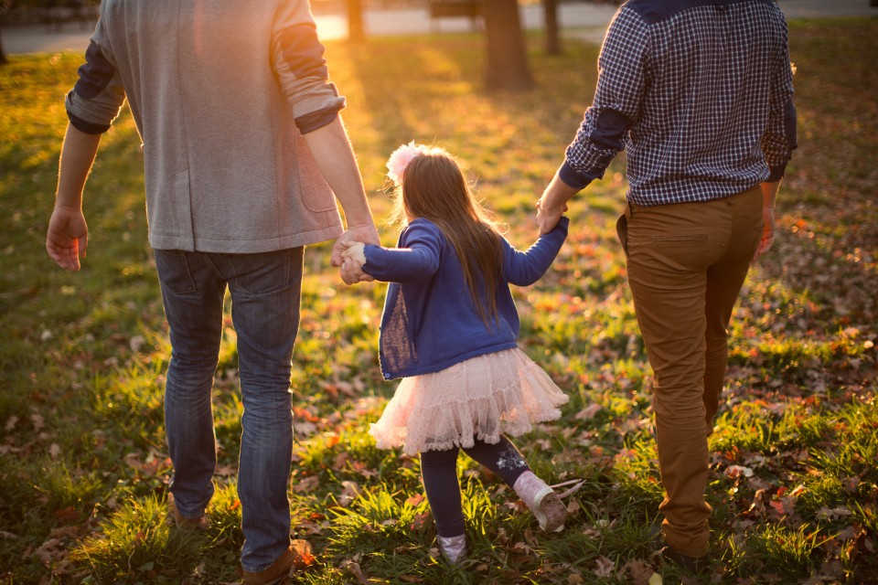Two parents holding hands with a child while walking through a park.